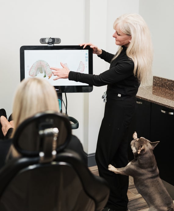 A photo of doctor shows to patient model of jaws on the screen