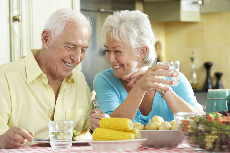 a picture of an older couple smiling at each other at the dinner table because they know what will affect the cost of their dental implant procedures.