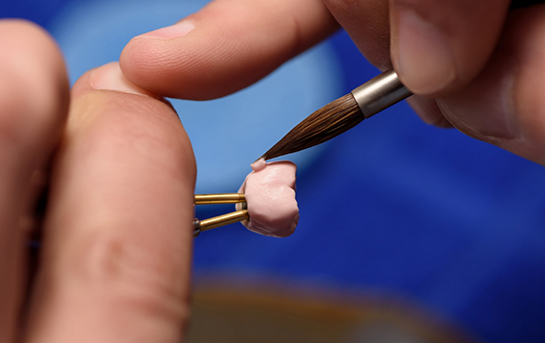 Dental lab worker carefully brushing a dental crown