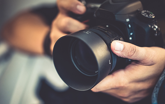 Close-up of hands holding a professional camera with a large lens