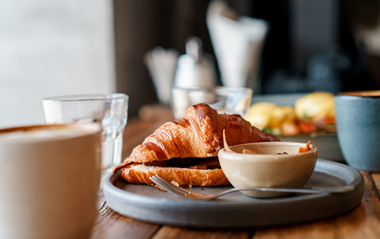 Croissant served on a plate with coffee and small dishes on a wooden breakfast table