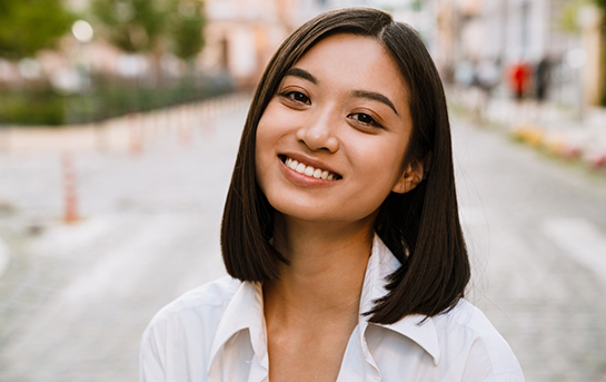 Young woman with dark hair smiling on a city sidewalk