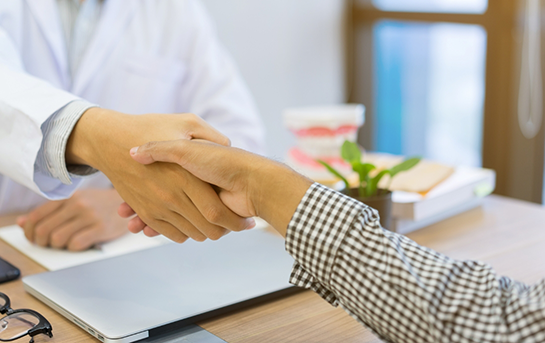 Person shaking hands with someone sitting across a table