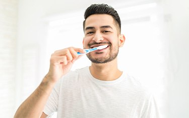 Man smiling while brushing his teeth