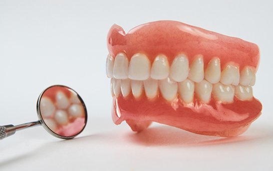 Set of dentures next to a dental mirror