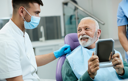 Senior dental patient looking at his new smile in a mirror